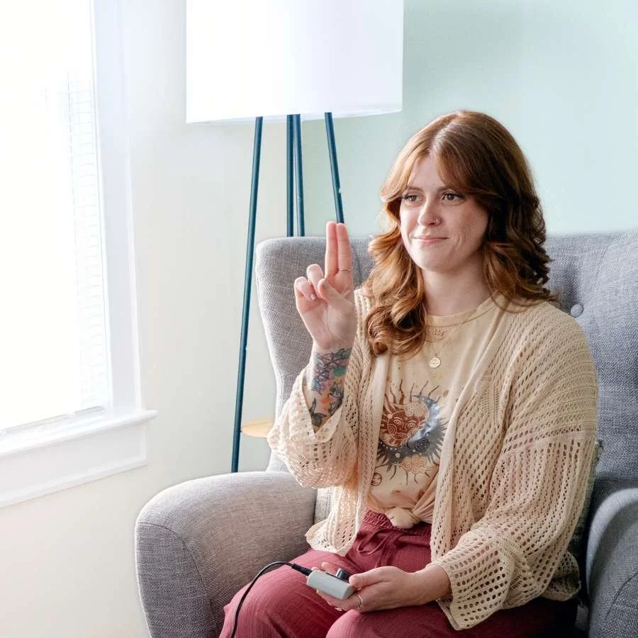 A Reset therapist demonstrates how EMDR thera is offered, holding up two fingers with one hand, and holding a Neurotek device in the other. 