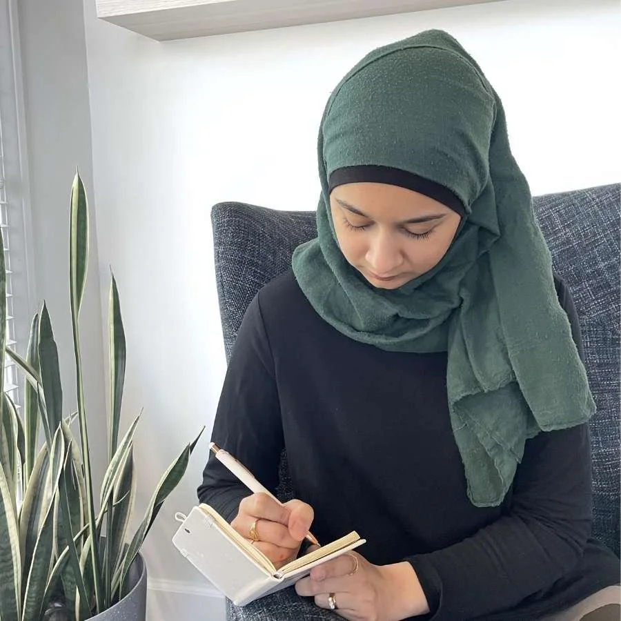 Someone wearing a green hijab writes in a journal.