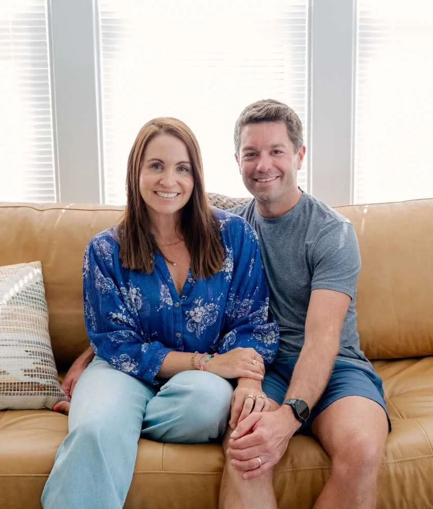 A smiling couple sits together on a leather couch