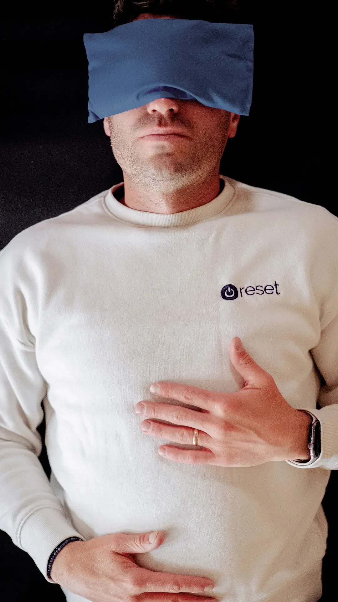A man wearing a Reset sweatshirt rests with his eyes covered