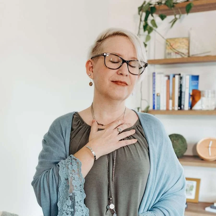 An older woman wearing glasses closes her eyes and breathes deeply.