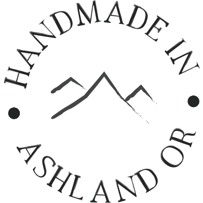 A circular logo with mountain graphics in the center and the text 'Handmade in Ashland, OR' around it.