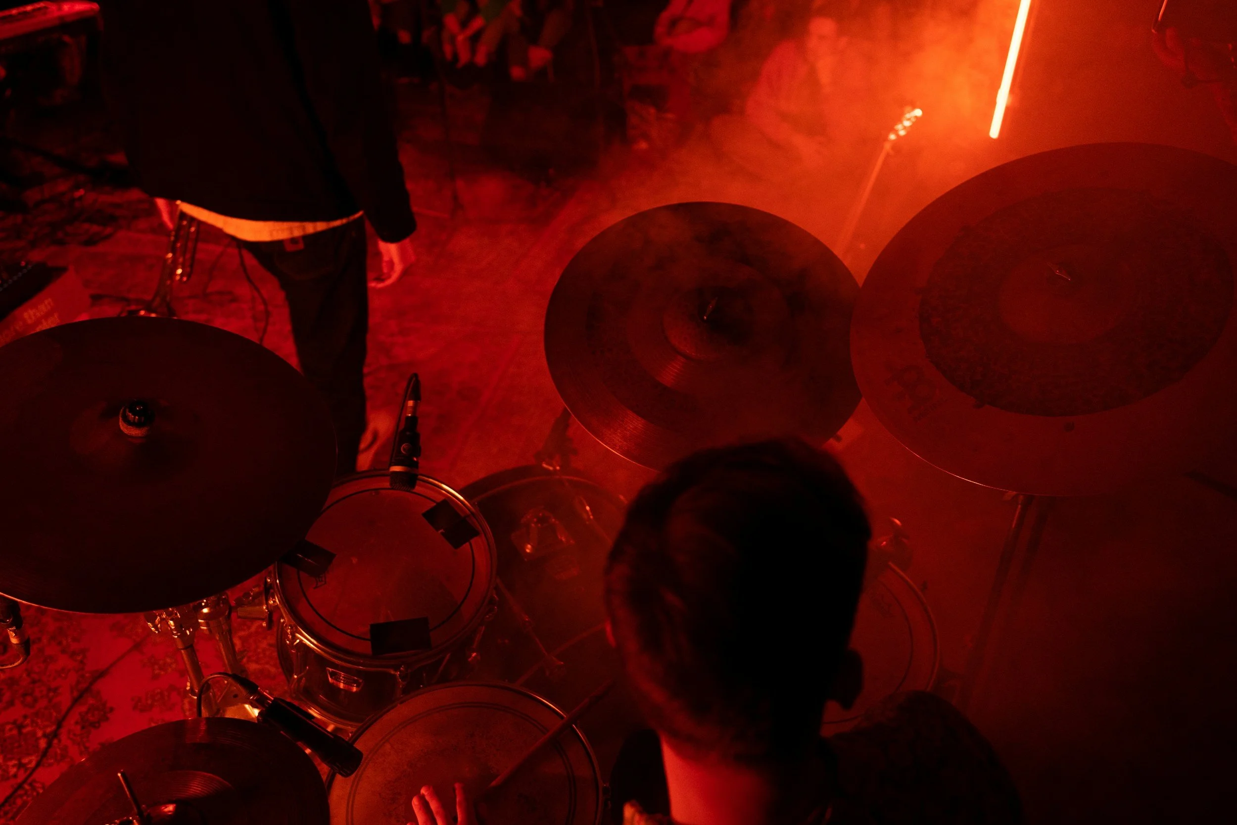 A top view of a music performance with a drum set and a person playing the drums, surrounded by red lighting and a smoky atmosphere.