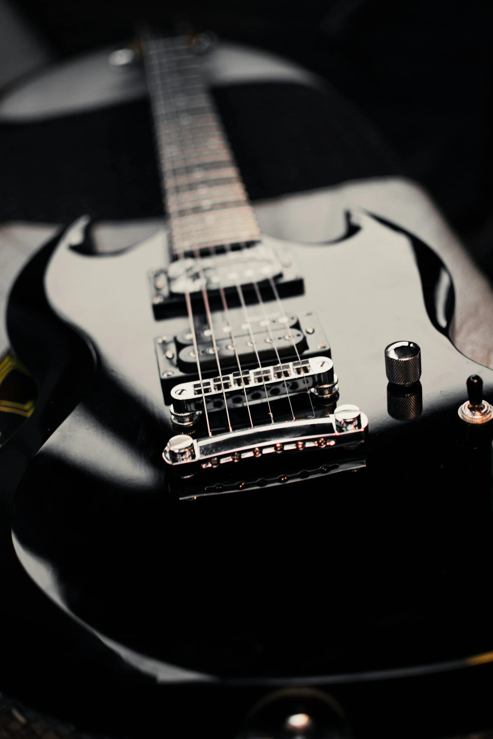 Close-up of a black electric guitar with chrome hardware, pickups, and a knob, resting on a soft surface.