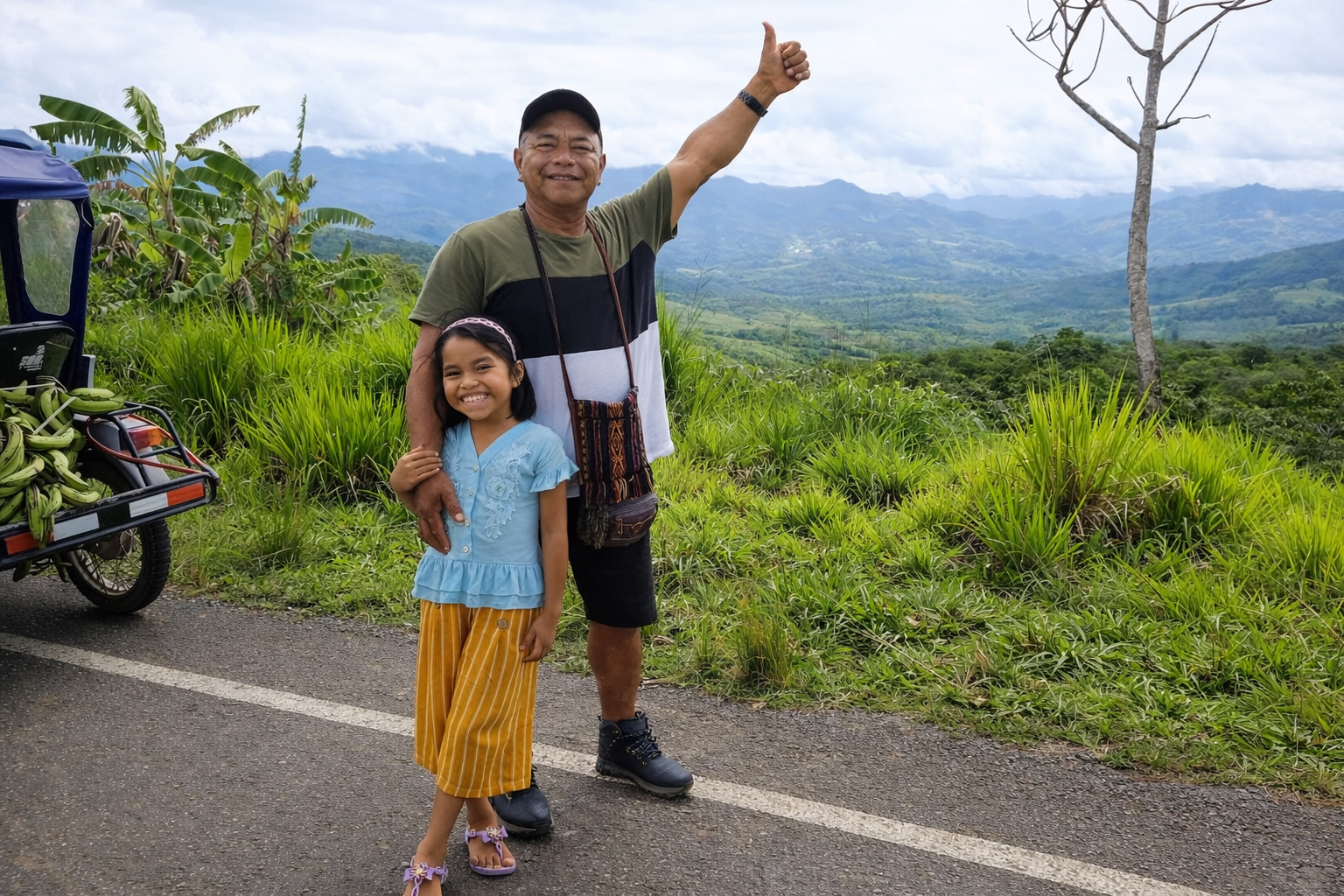 A man and a young girl smiling and standing together on a roadside with lush green hills and mountains in the background. The man has his arm raised in a thumbs-up gesture, and a tuk-tuk filled with bananas is visible on the left side.