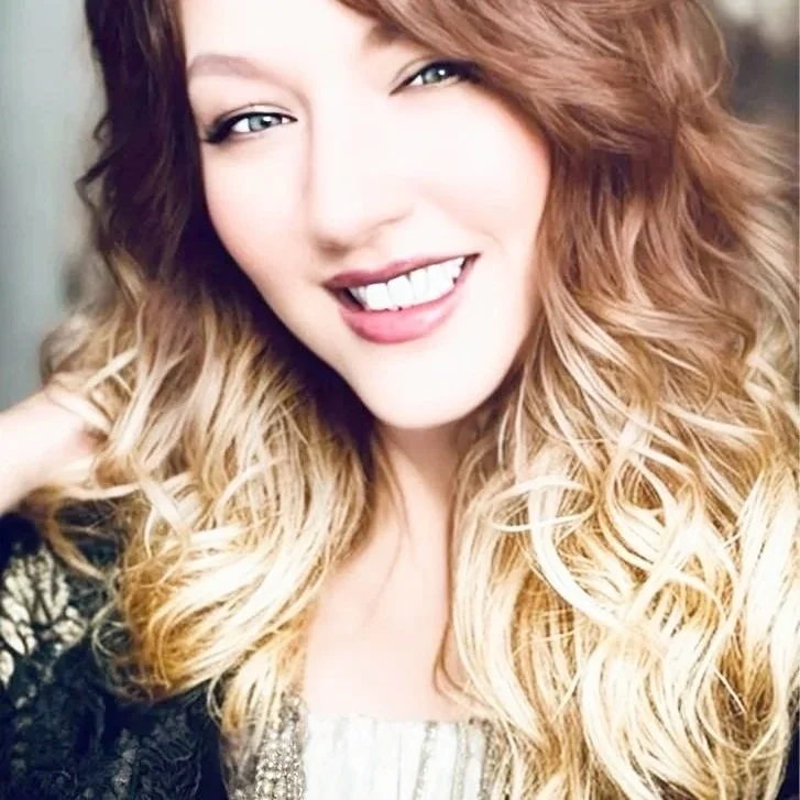 Close-up of a smiling woman with wavy blonde hair, showing her teeth and winking at the camera.