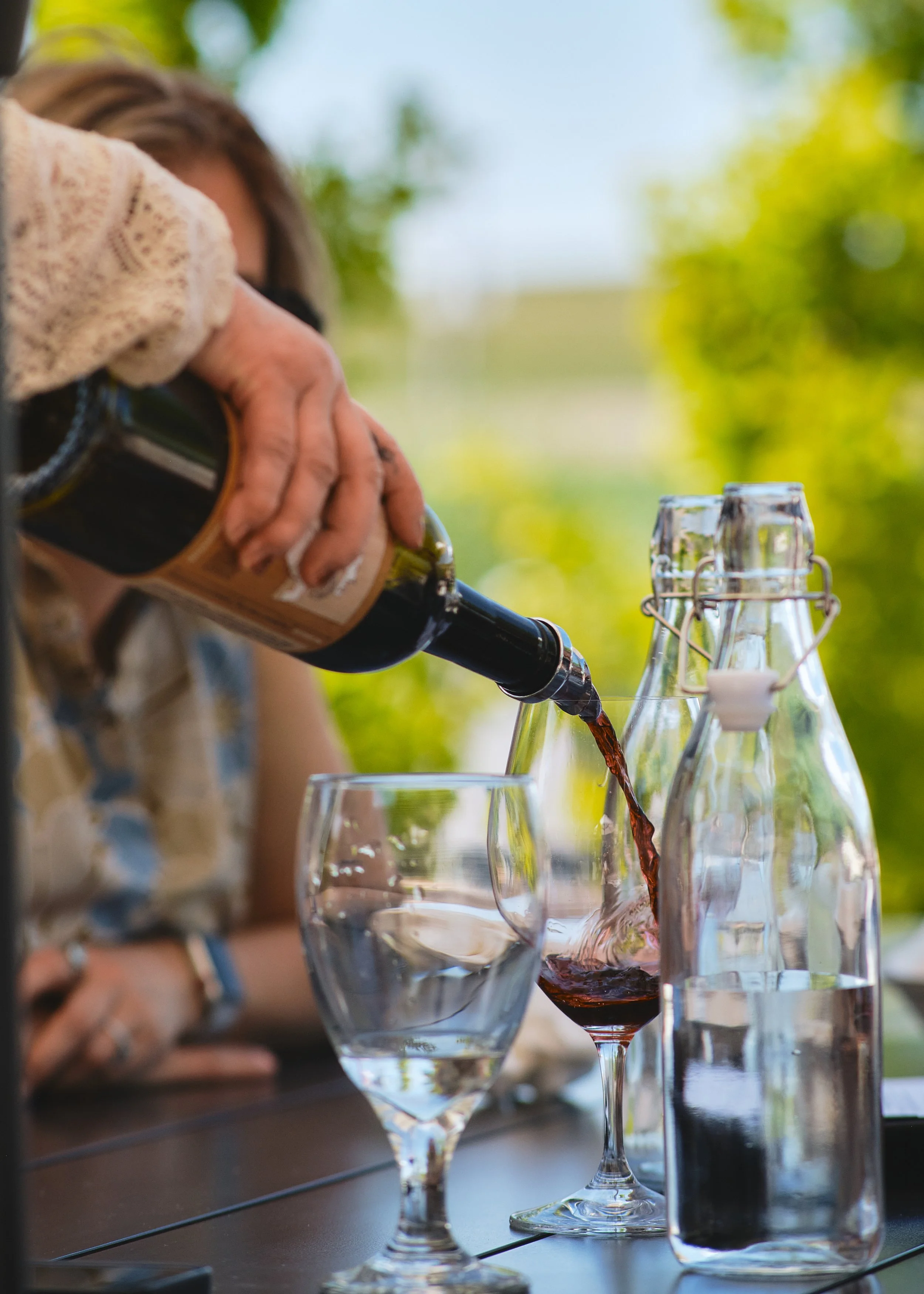Woman pouring red wine outdoors beside glass water bottles