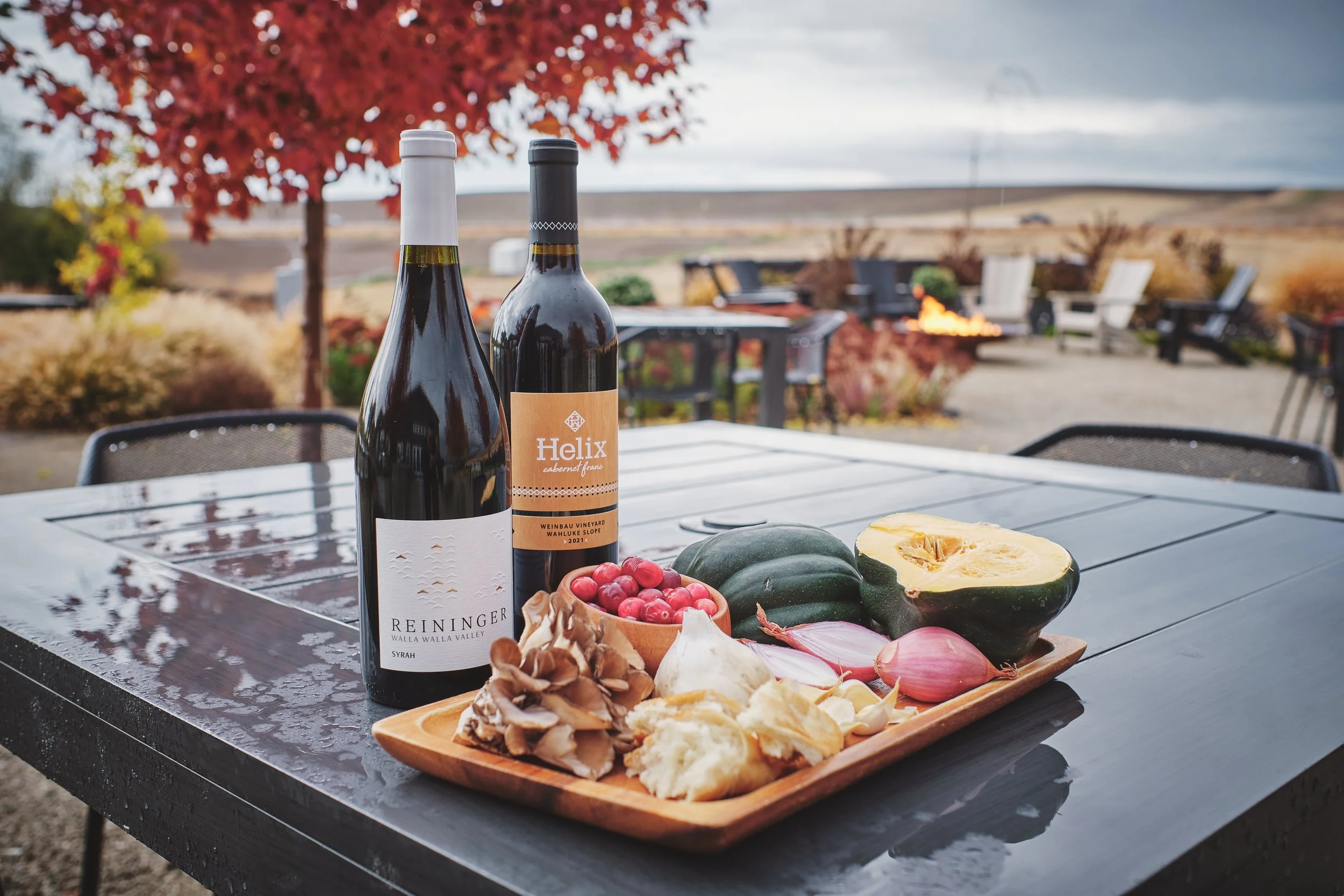 Two wine bottles with a fall harvest board of squash and mushrooms on a winery patio