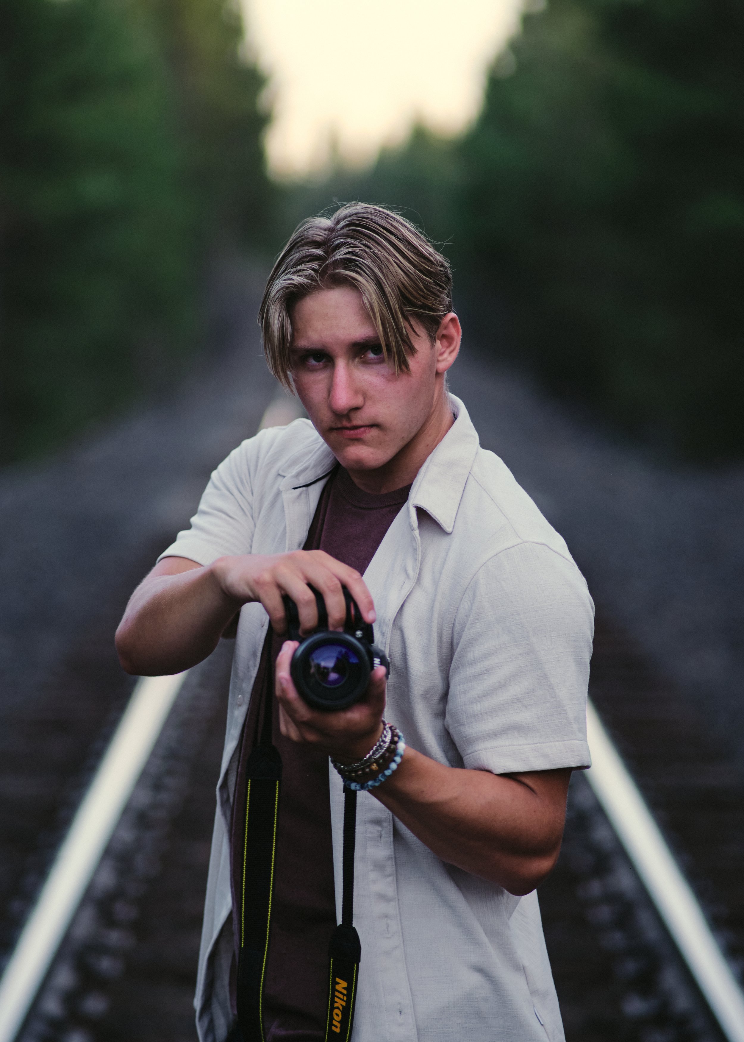 Young man holding a camera on railroad tracks