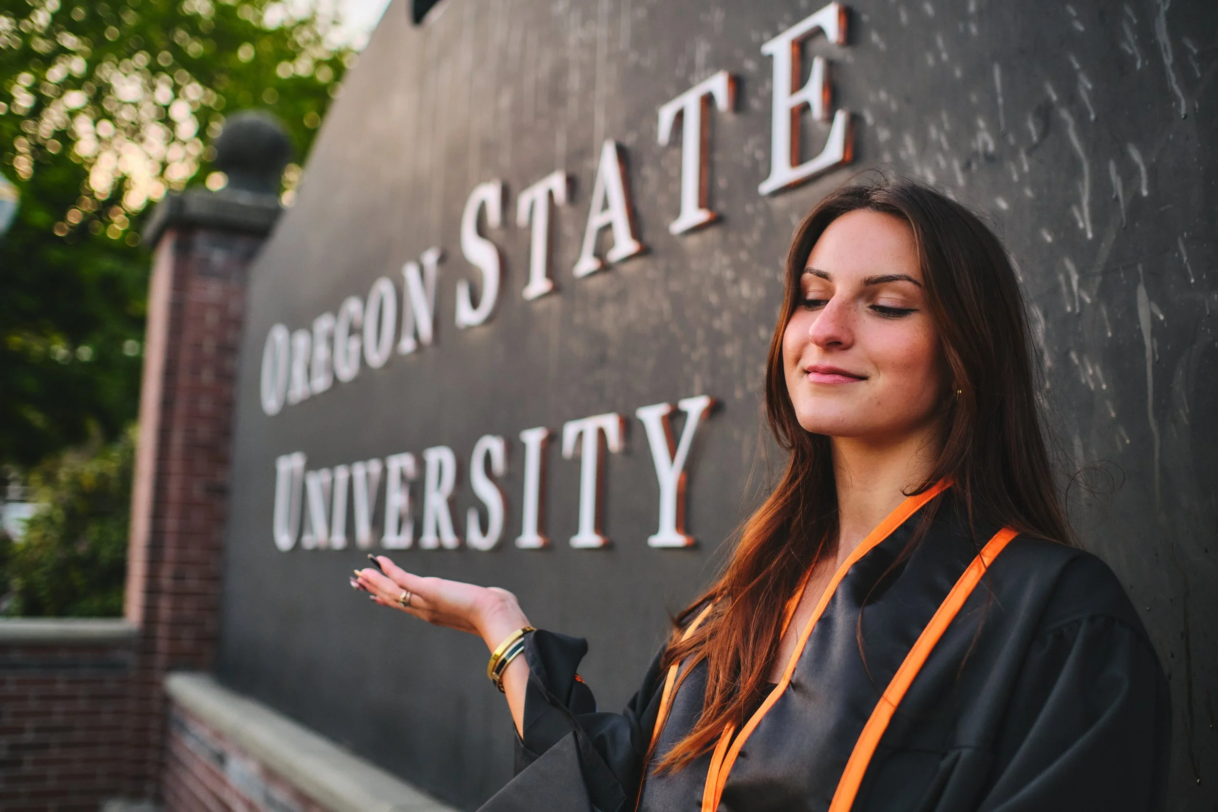 Oregon State University graduate beside the OSU sign in Corvallis