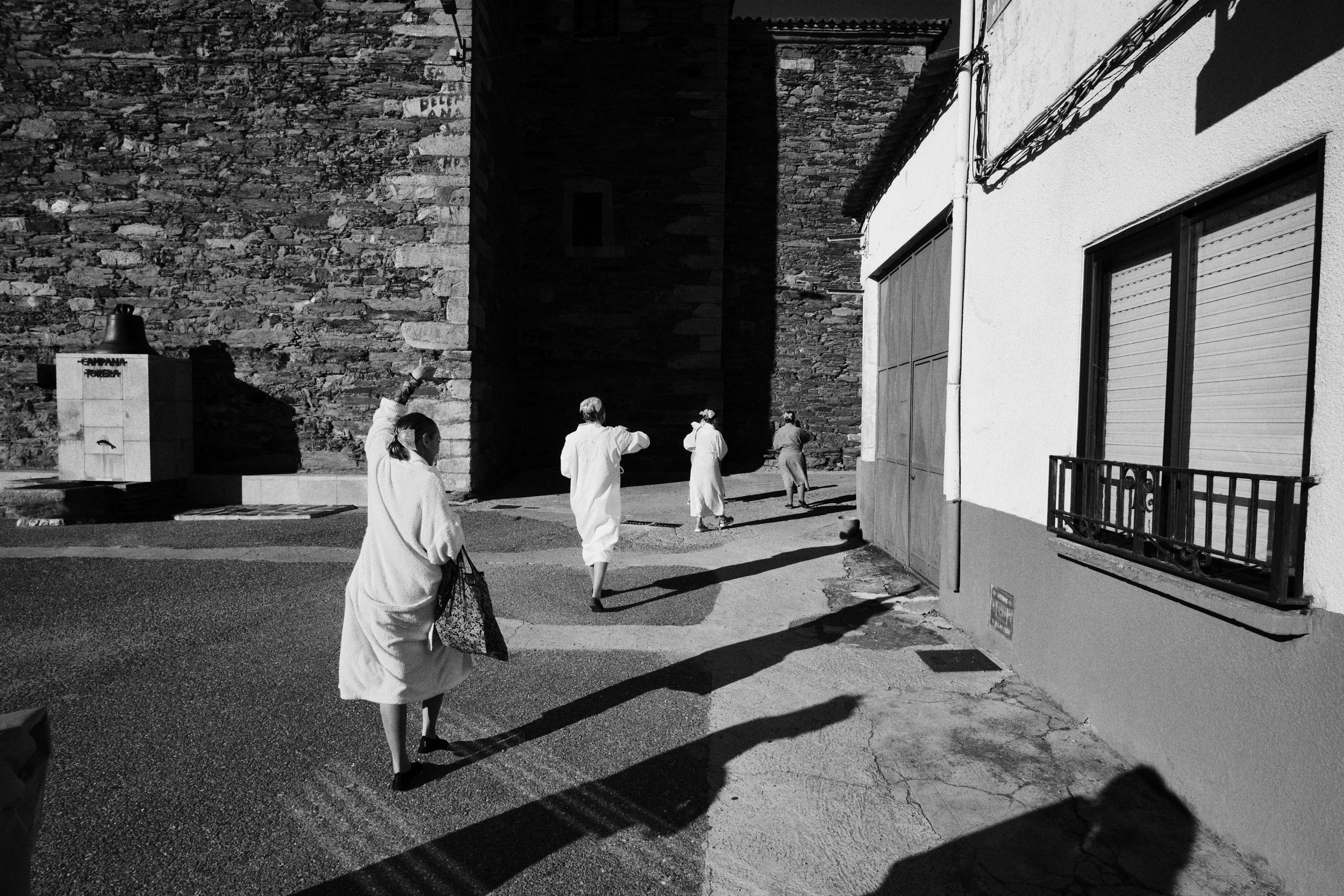 Black and white photo of women in white robes walking a village street in Spain