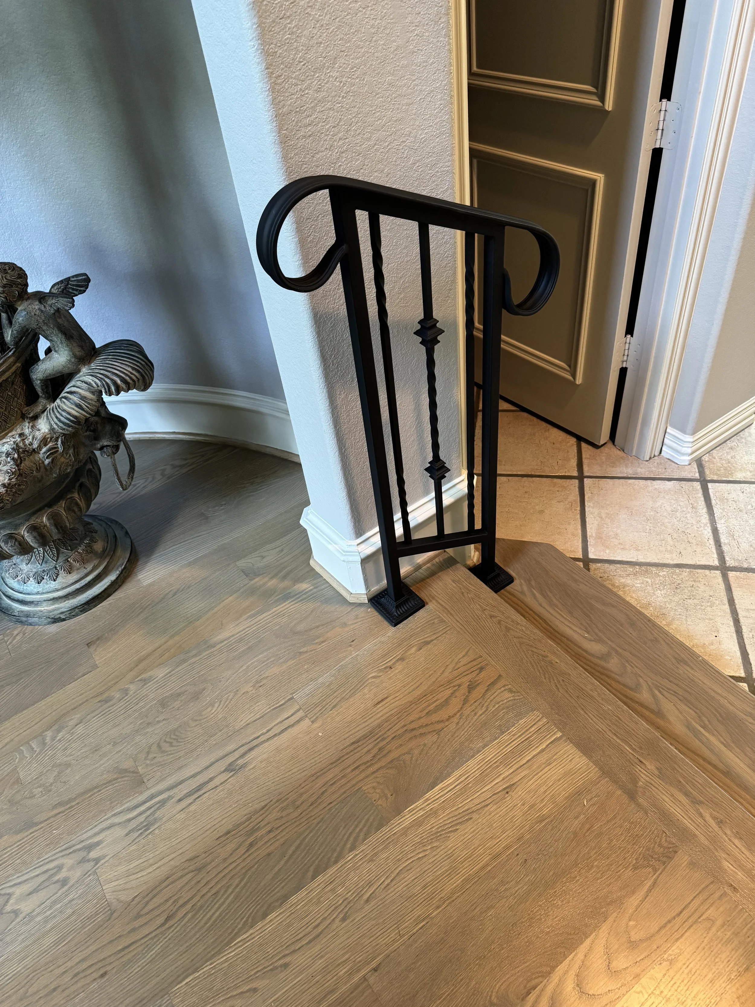 Part of a staircase with a black metal railing, a section of a room with wooden flooring, a decorative statue of a cherub, and a partially open door.