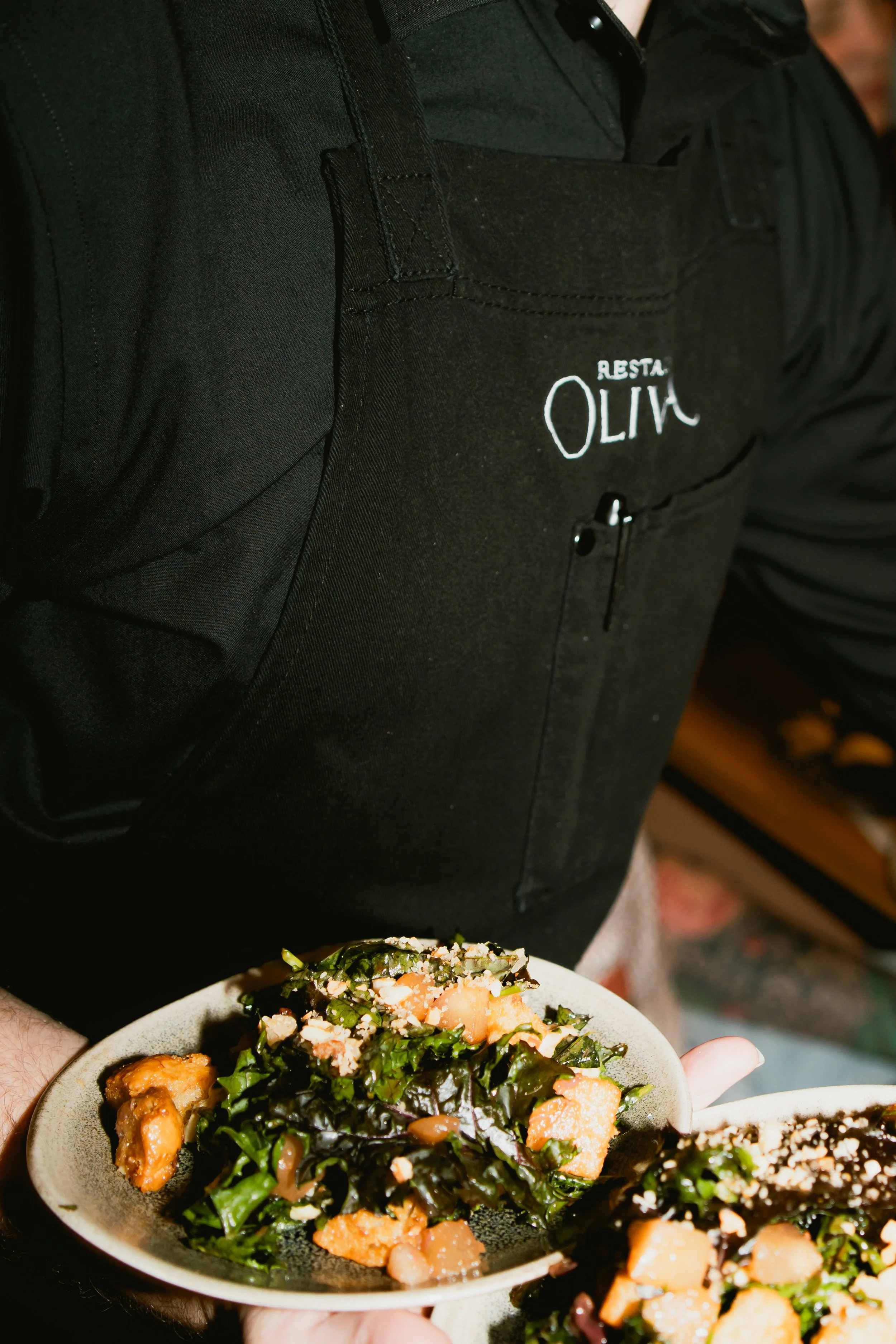 Person holding two plates of salad with greens, orange pieces, and sesame seeds in a restaurant setting.