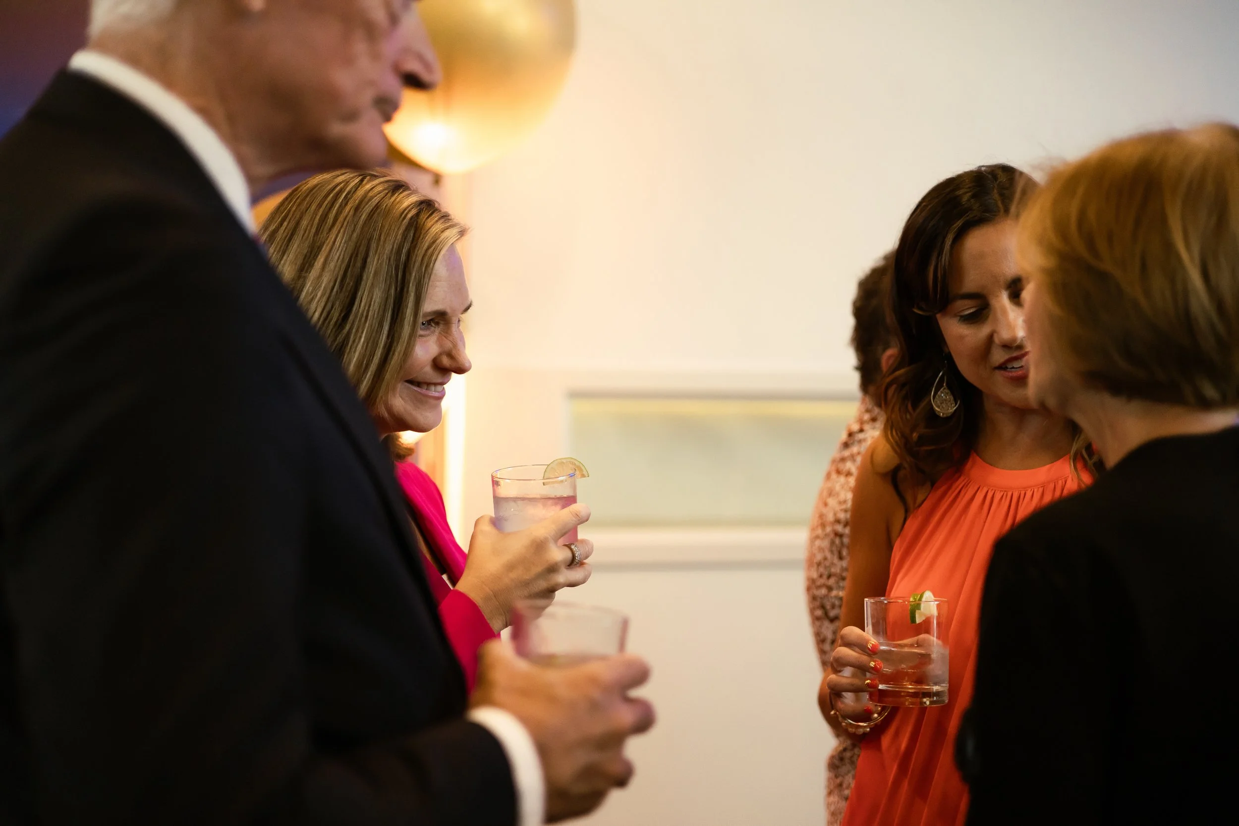 People socializing at a party, holding drinks, indoors with warm lighting.