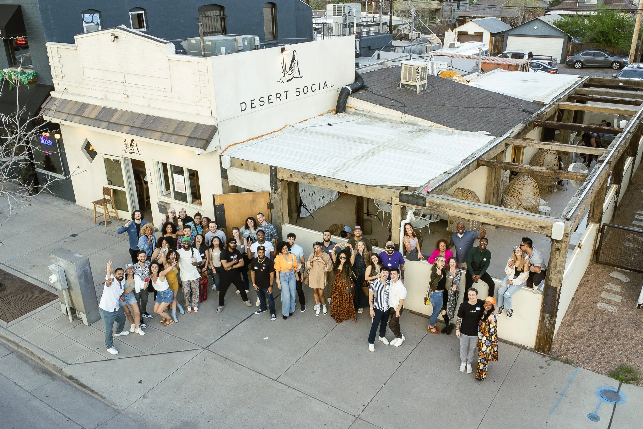 A large group of people gathered outside a restaurant named Desert Social, posing for a photo on the sidewalk.