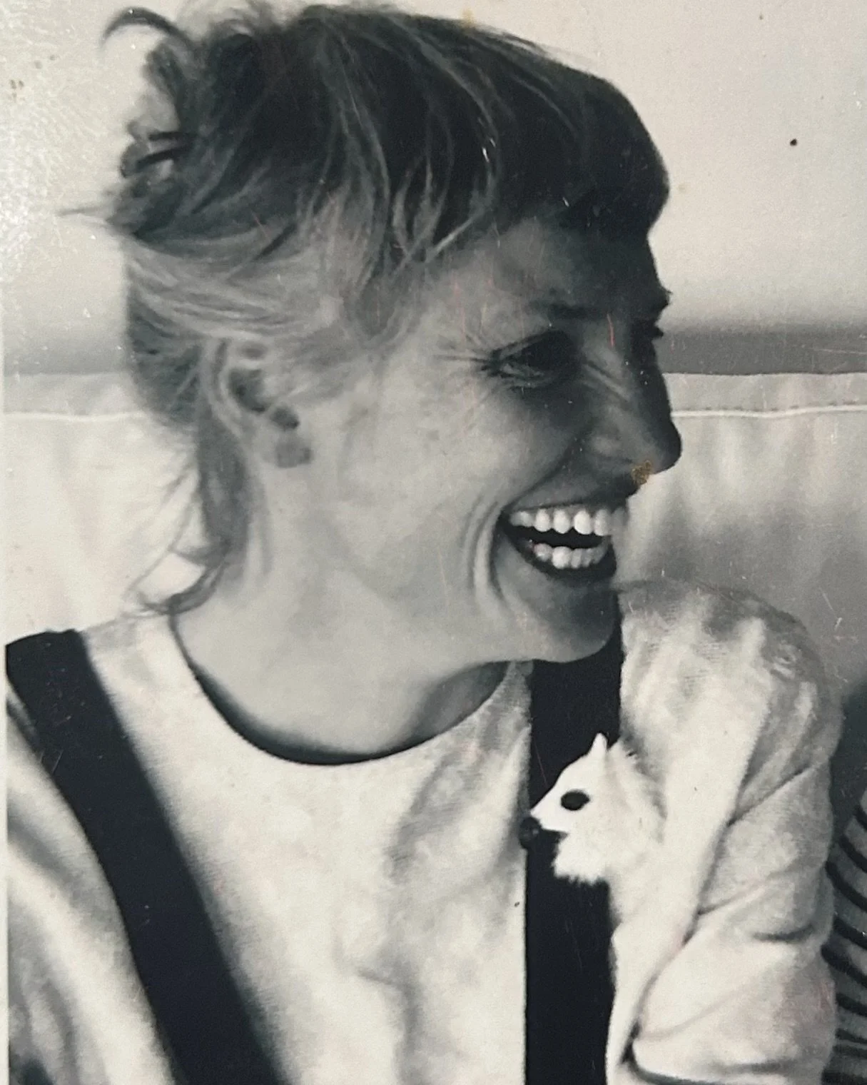 Black and white photo of a woman with short hair smiling and looking to her right, holding a small dog.