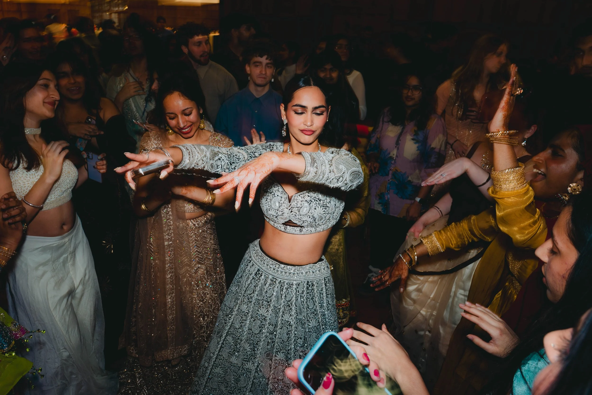 A woman dressed in a traditional Indian outfit, surrounded by people at a festive celebration.
