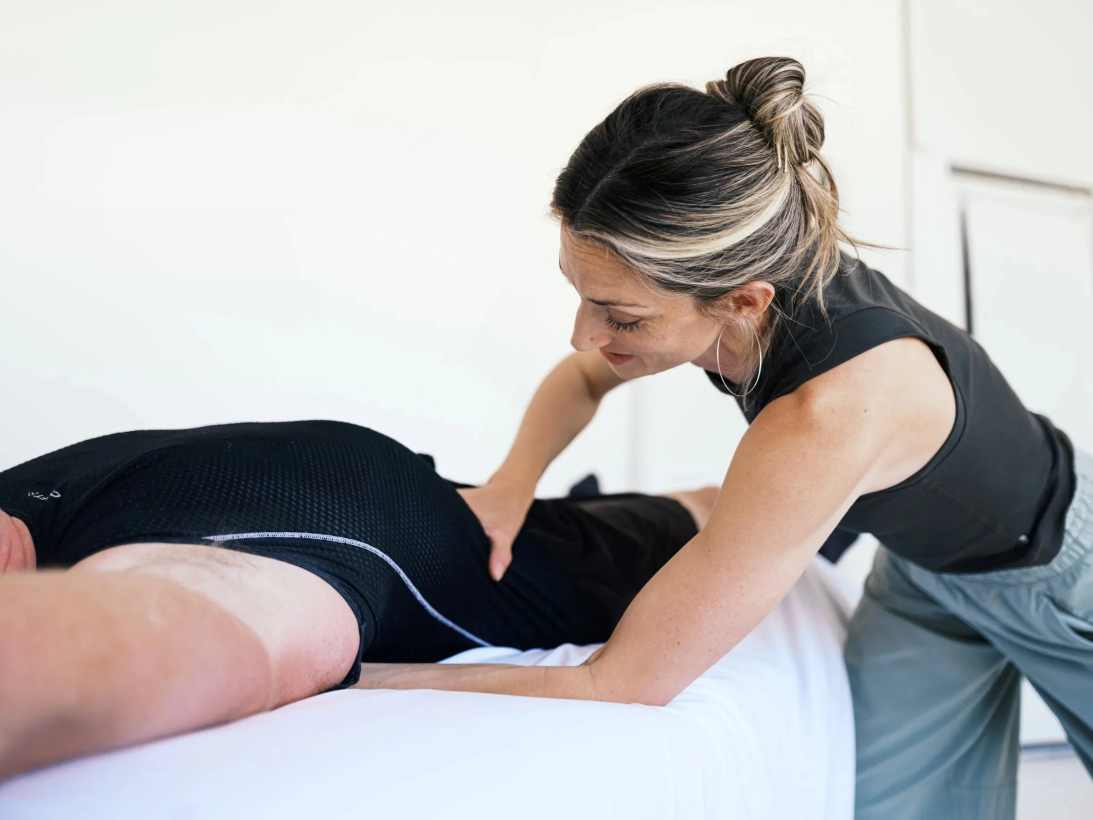 A woman performing a massage therapy technique to relieve back pain to a man lying on a massage table.