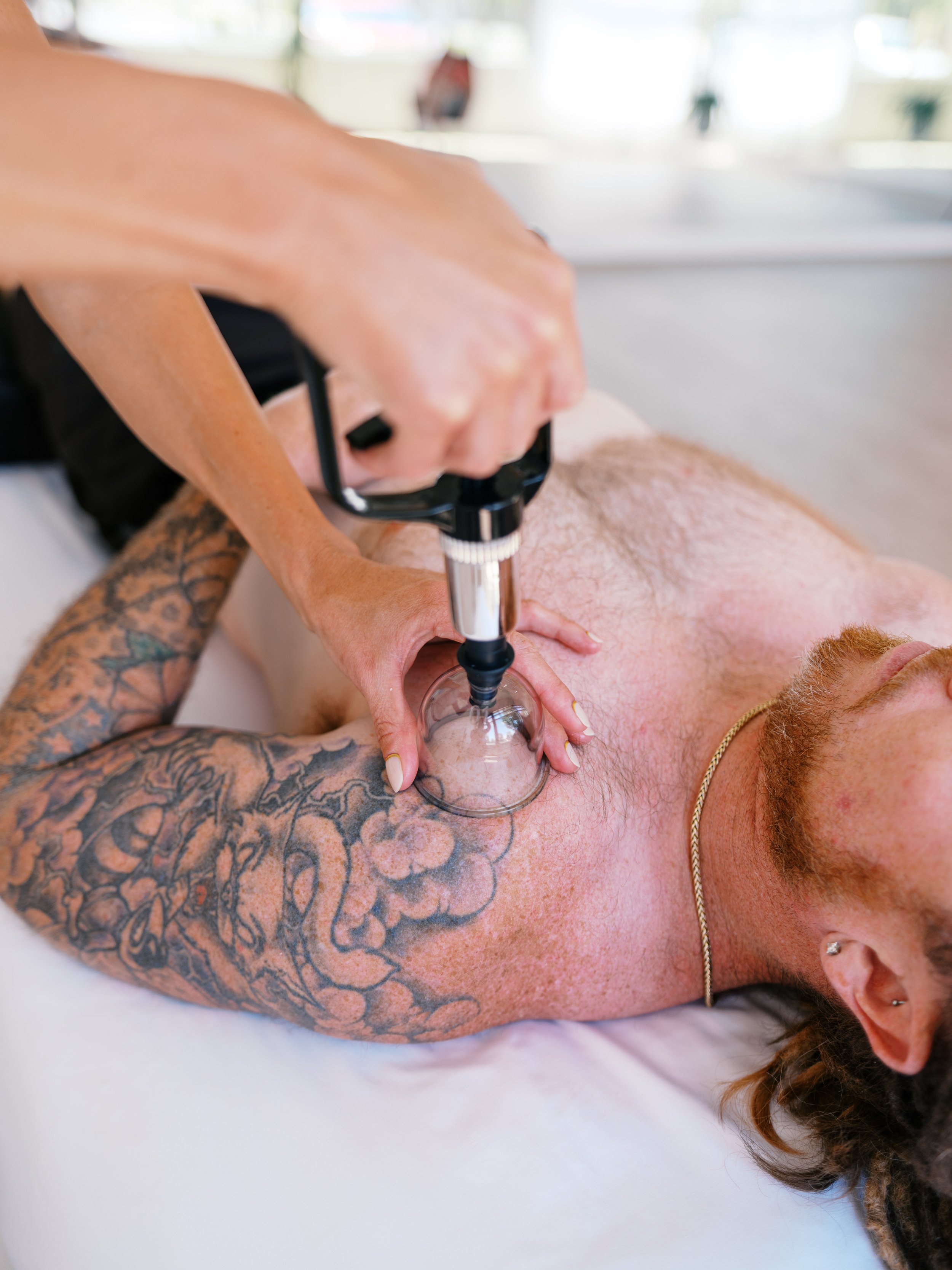 A woman in athletic clothing performing massage therapy cupping on a man lying.