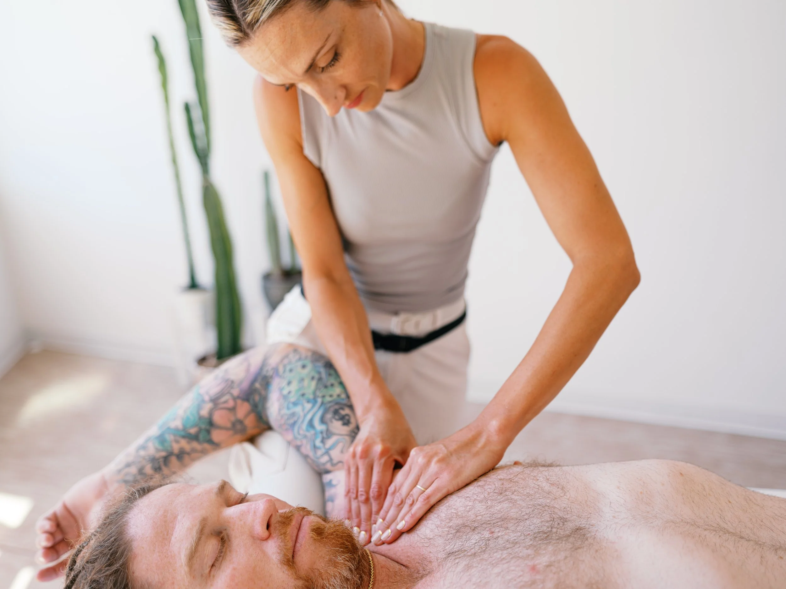 A woman performing a massage therapy technique to relieve back pain to a man lying on a massage table.