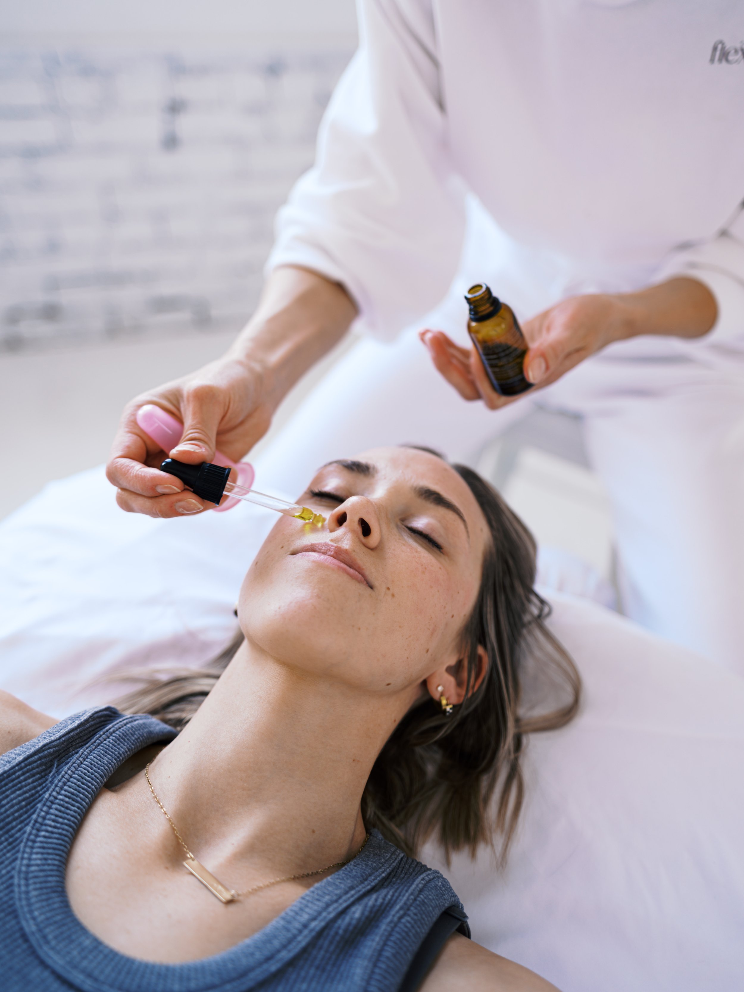 A woman receiving facial cupping treatment from a practitioner in a bright, modern clinic with large windows.