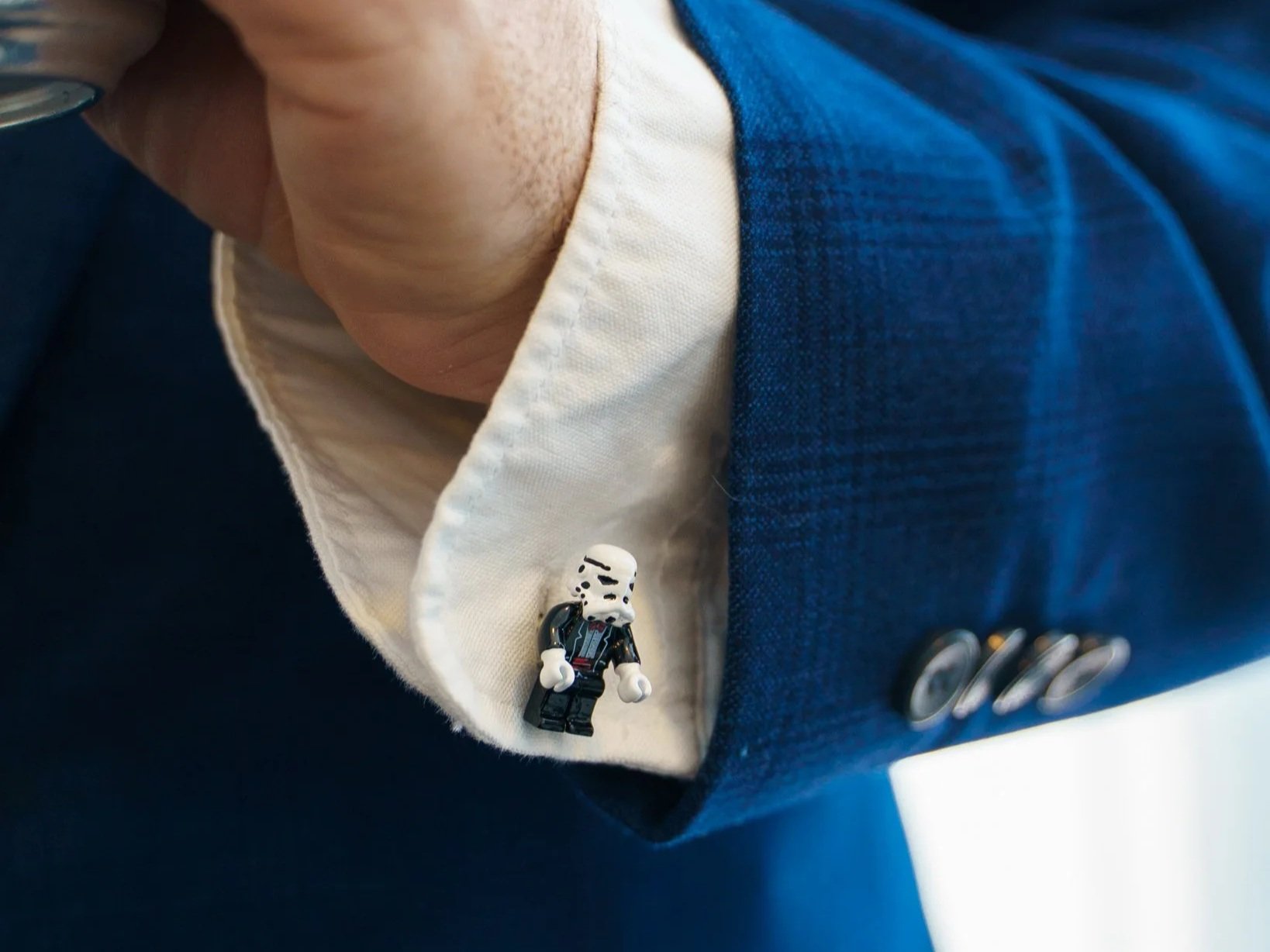 Close-up of a person's outfit, showing a white shirt with a Lego Star Wars Stormtrooper figure pin attached, and a dark blue blazer with metallic buttons.