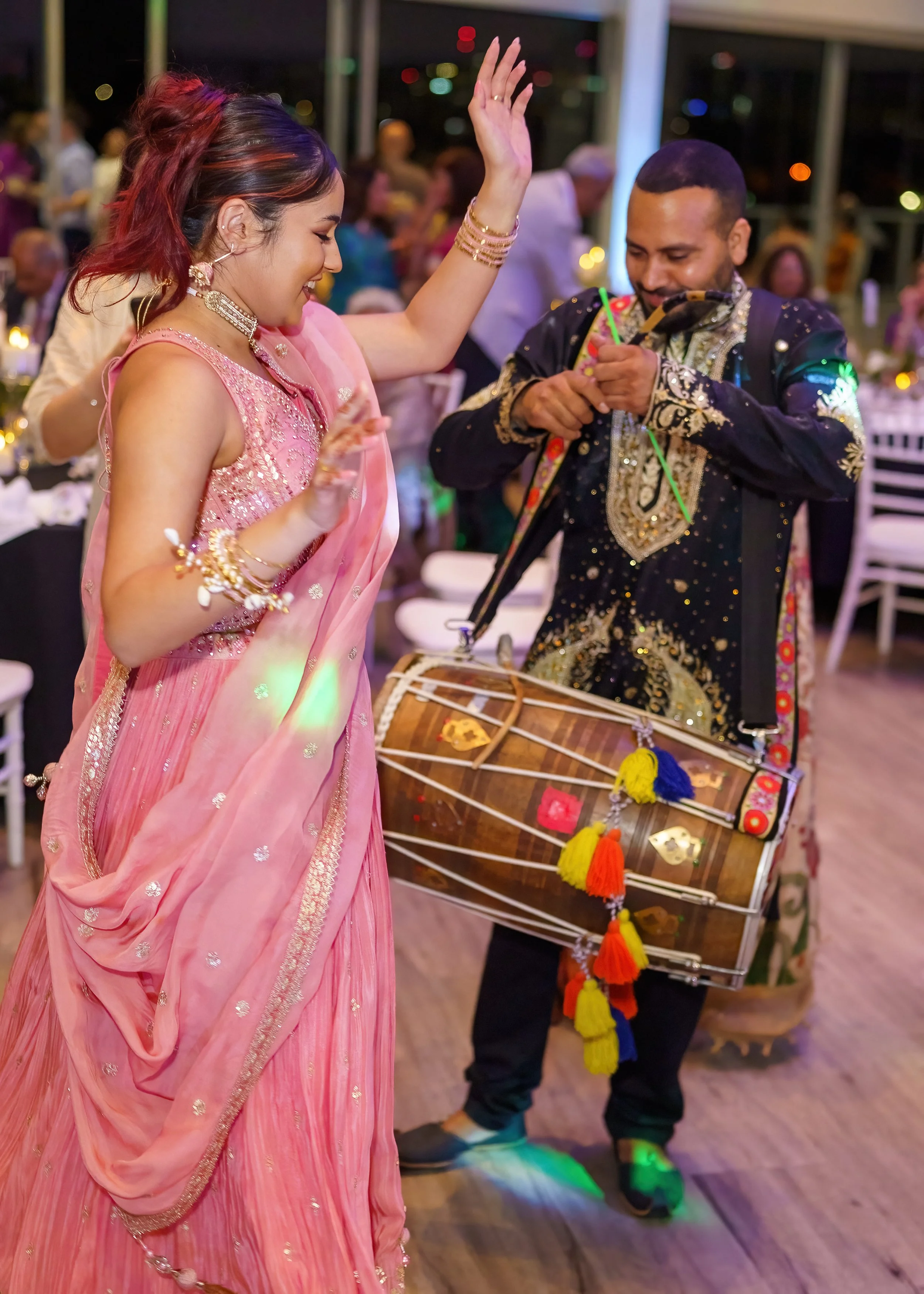 A woman in a pink traditional dress dancing with a man who is playing a drum at a celebration or party.