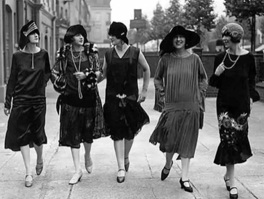 Black and white image of five women in Western 1920s garb walking on a wide sidewalk