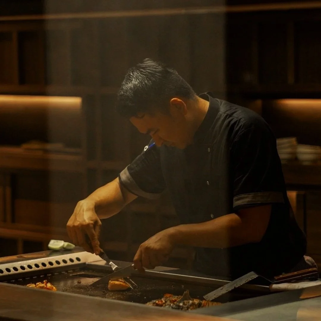 A chef cooking on a grill in a dimly lit kitchen.