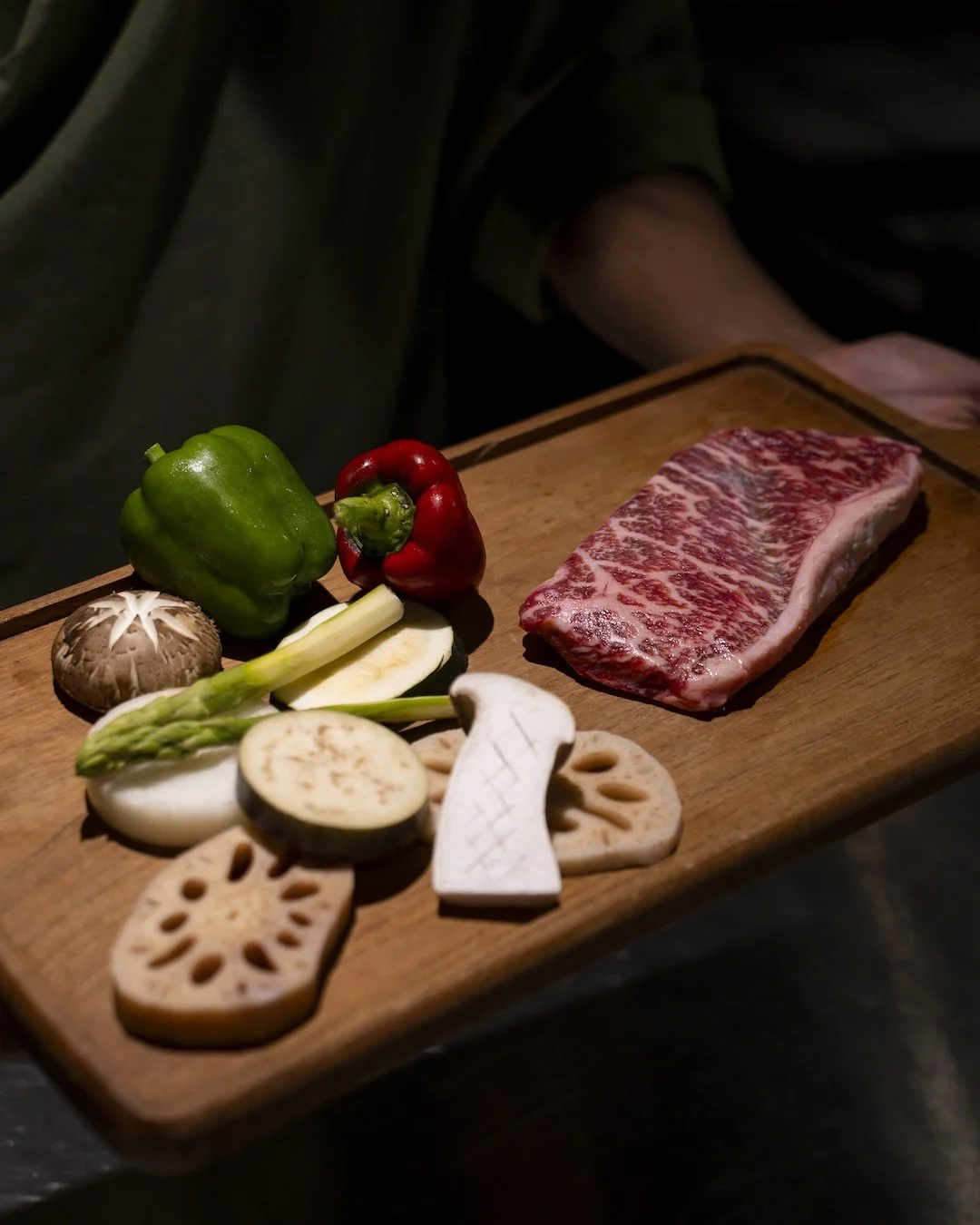Wooden board with raw marbled beef, bell peppers, shiitake mushroom, asparagus, eggplant, lotus root, and other vegetables.