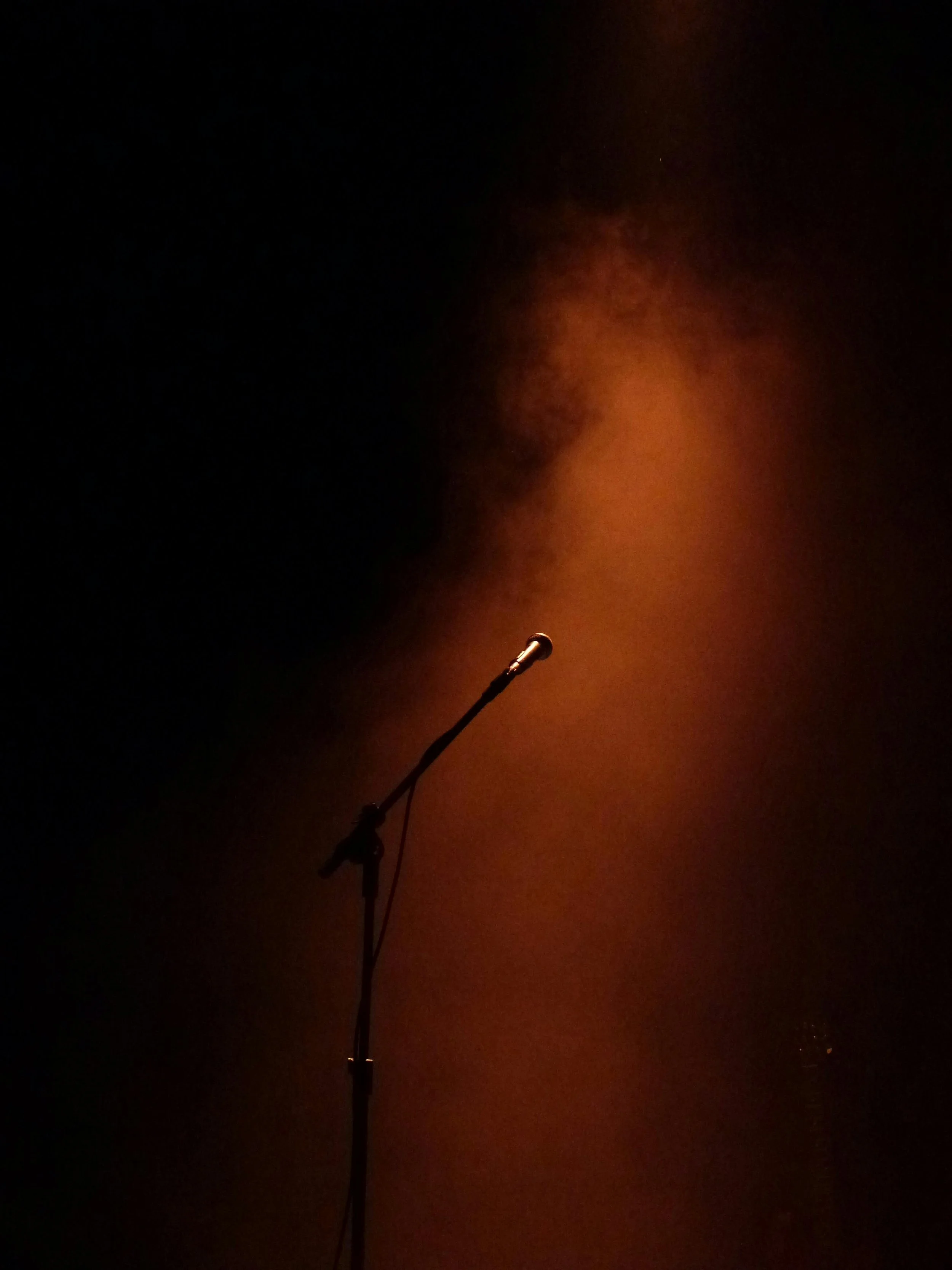 Stage microphone illuminated by warm amber spotlight in darkened performance venue