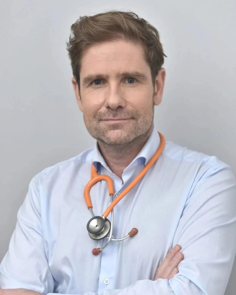 Médecin homme avec une blouse blanche et un stéthoscope orange autour du cou, portrait en studio.
