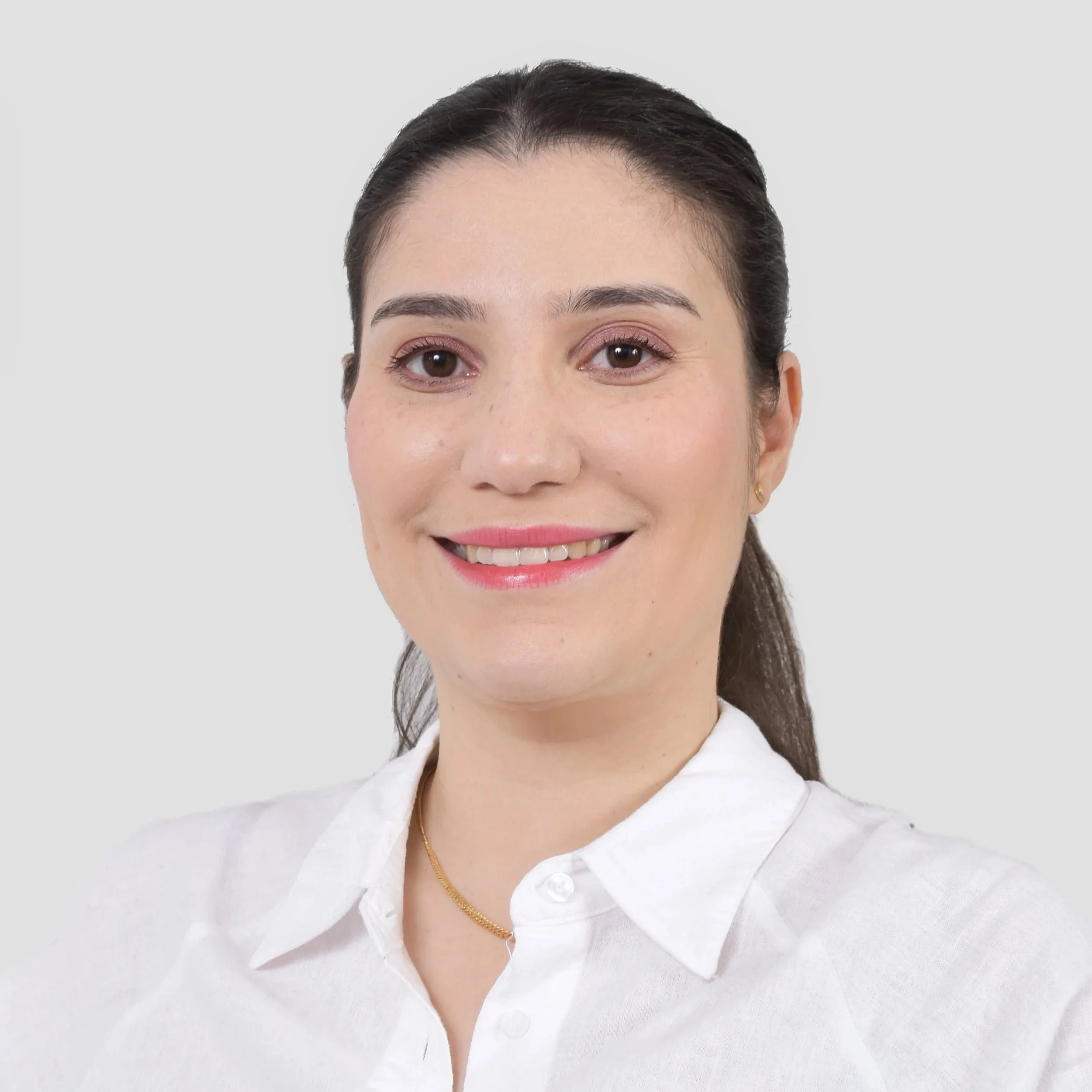 Portrait d'une femme souriante avec une chemise blanche et un fond gris clair.