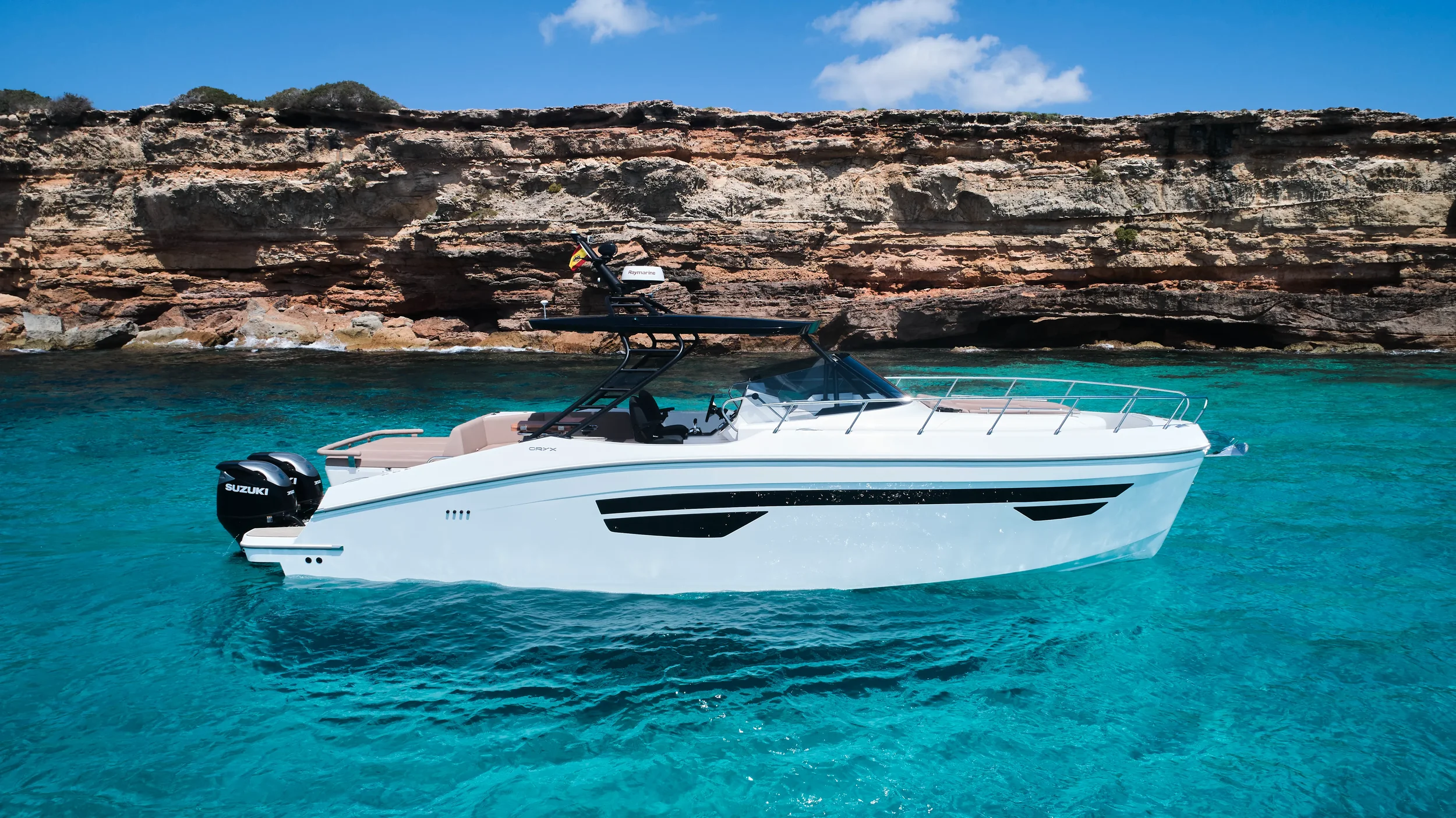 Oryx 38 Santa Cruz cruising along cliffs with bright turquoise water in Ibiza