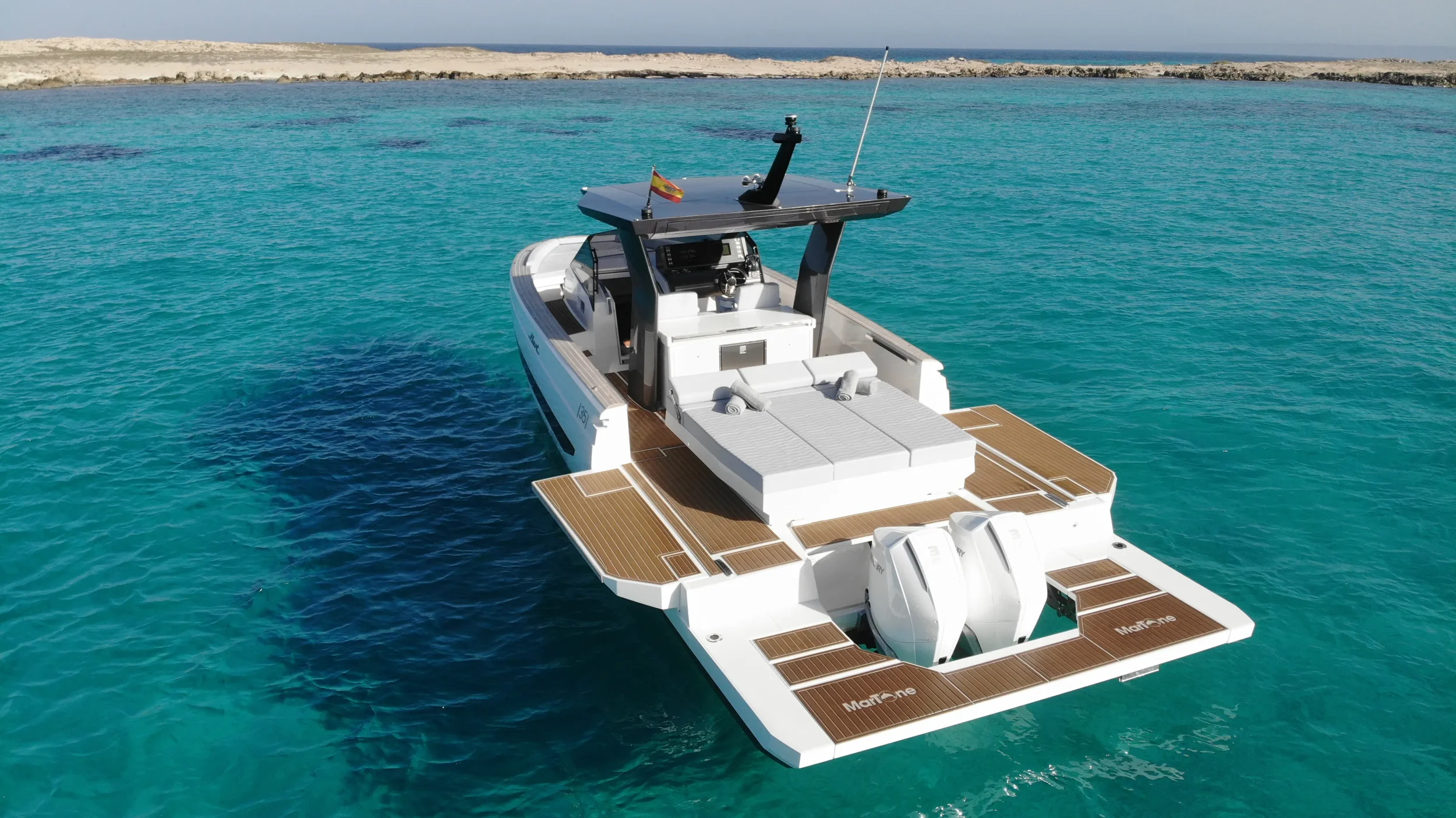 Rear-angle shot of the Fiart 35 Martone W floating in calm turquoise water with the large stern sunbed and open deck layout.