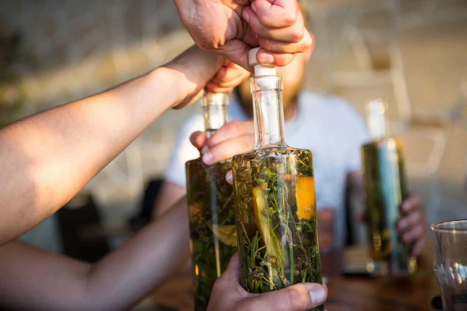 Hands holding bottles of herb-infused oil with cork tops being opened