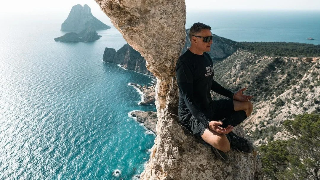 Man meditating on cliff overlooking sea and islands