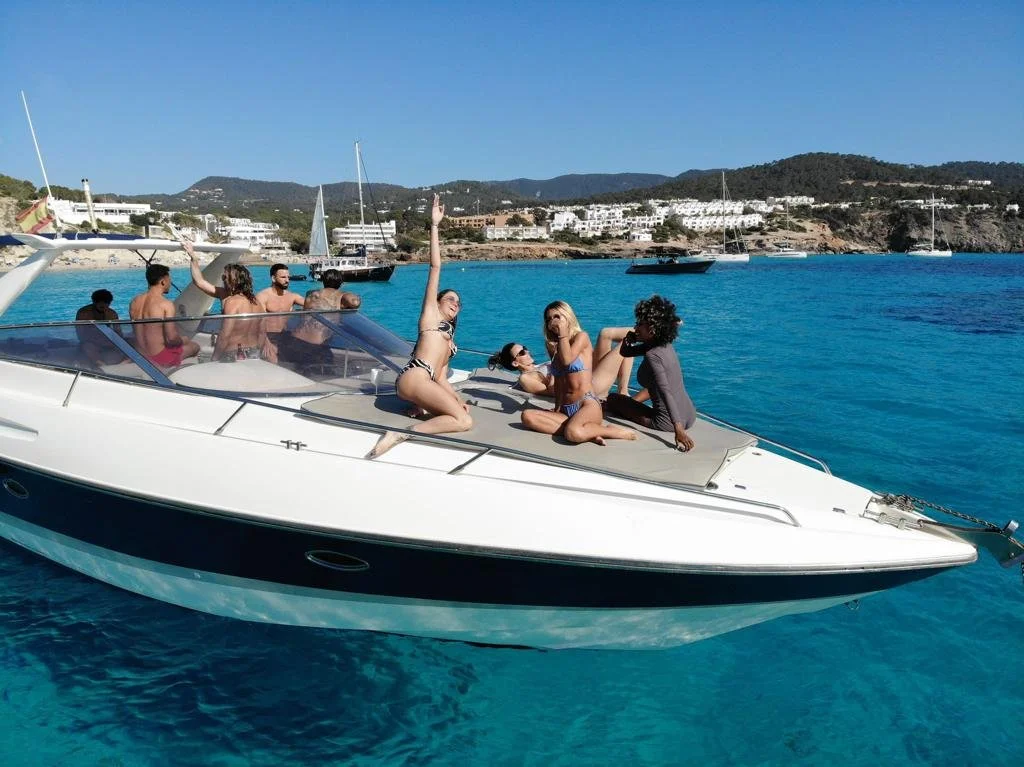 Group of people on a yacht in clear blue water, with a scenic view of the coastline in the background.