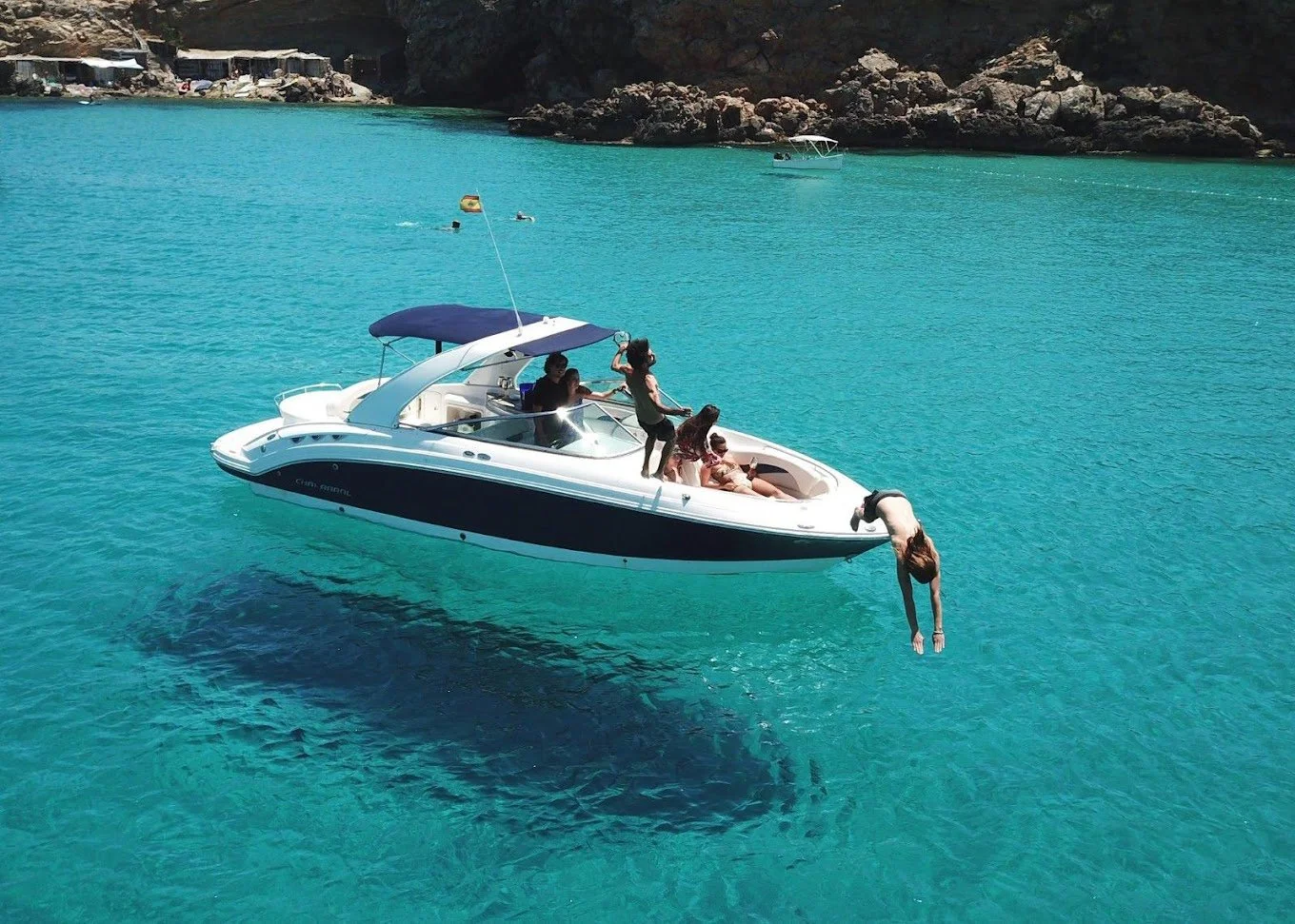 People on a motorboat in clear blue water, with a person diving off the front.