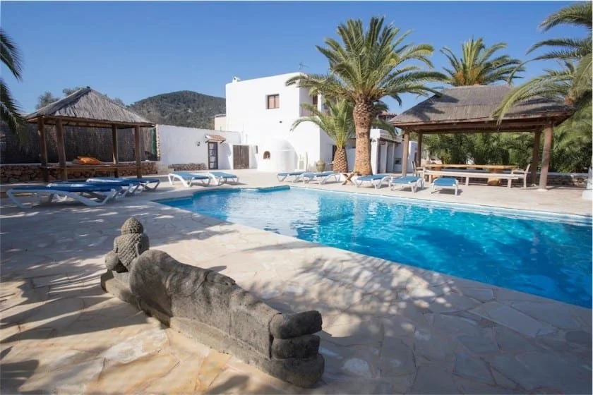 Outdoor pool area with palm trees, sun loungers, and a thatched-roof pergola.