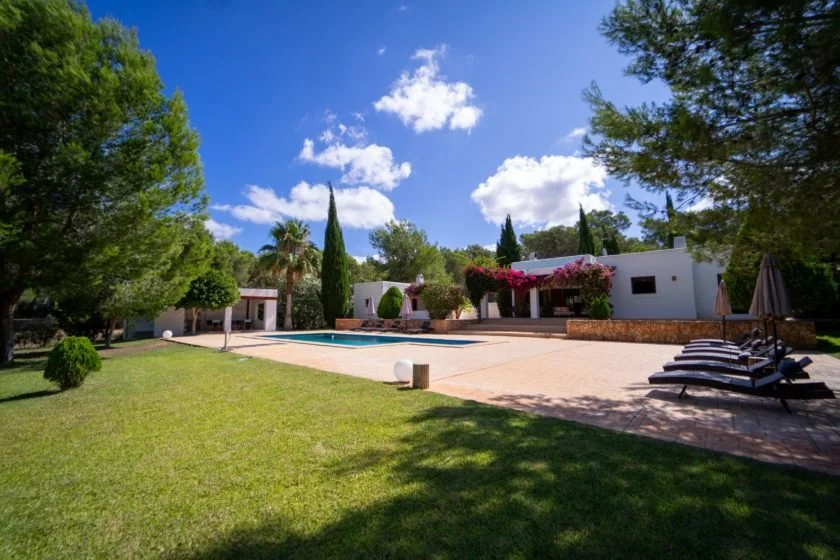 Luxury villa with pool, loungers, garden, trees, and blue sky.