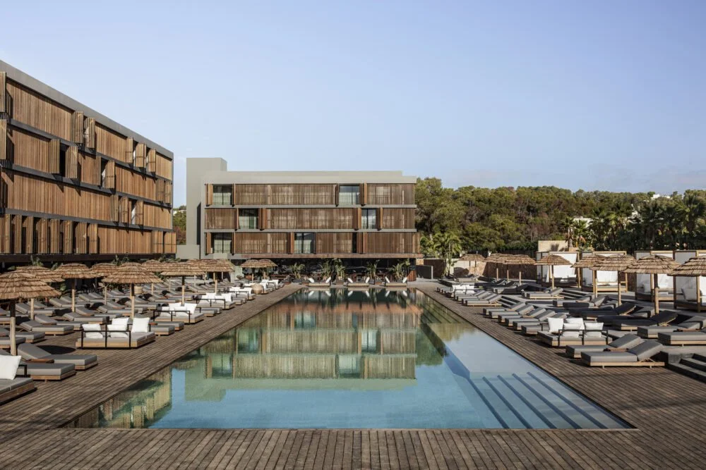 Modern hotel exterior with symmetrical pool, sun loungers, and parasols