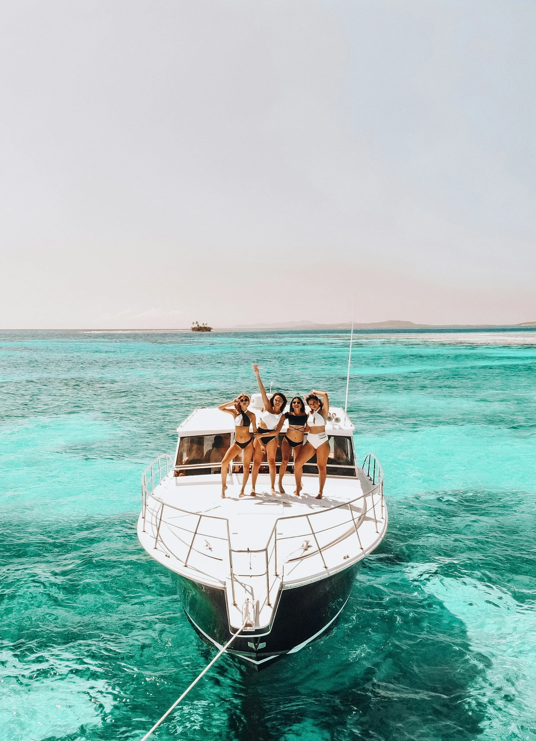 Four women in swimsuits on a boat in turquoise water.