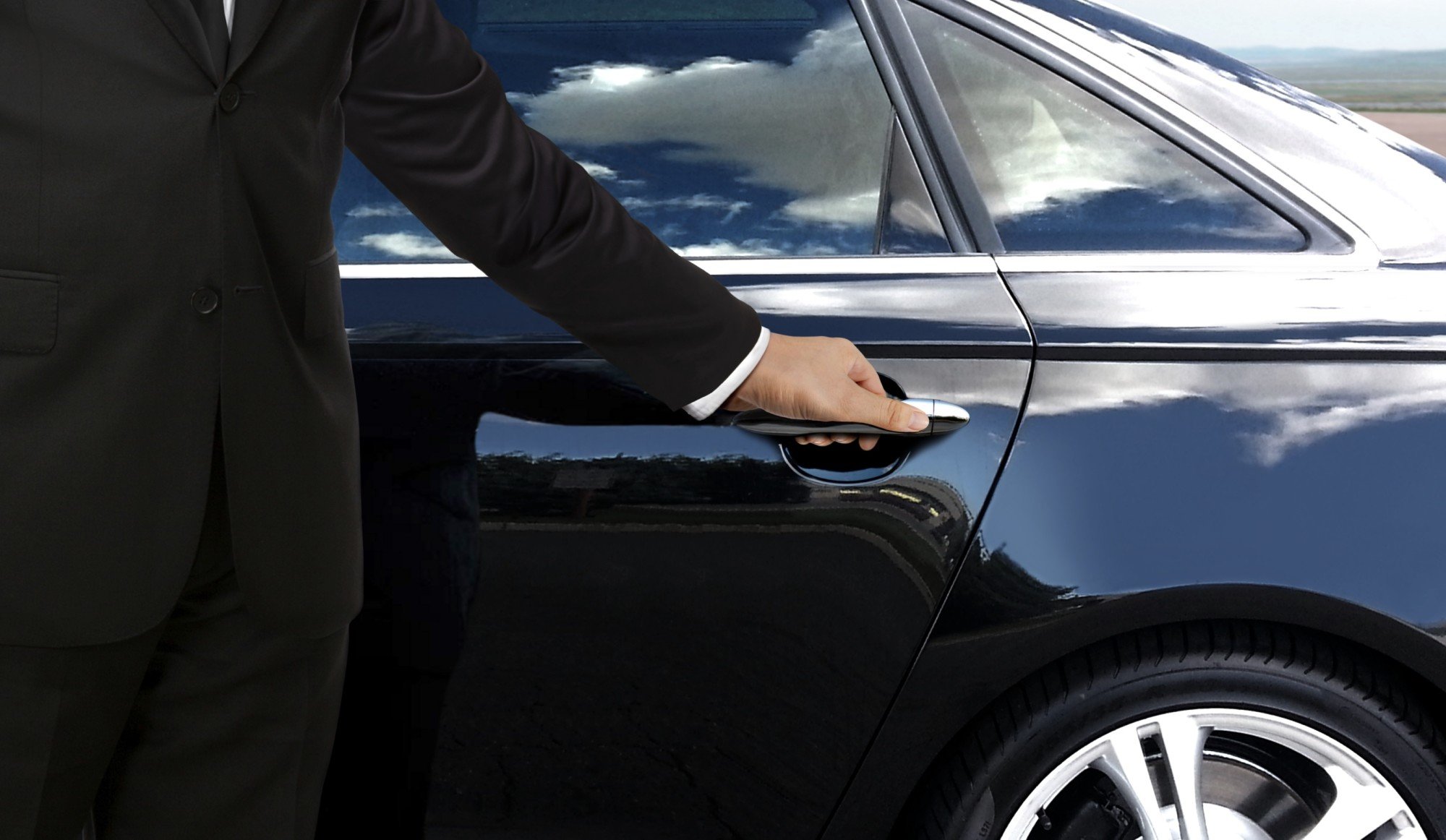 Person in black suit opening luxury car door