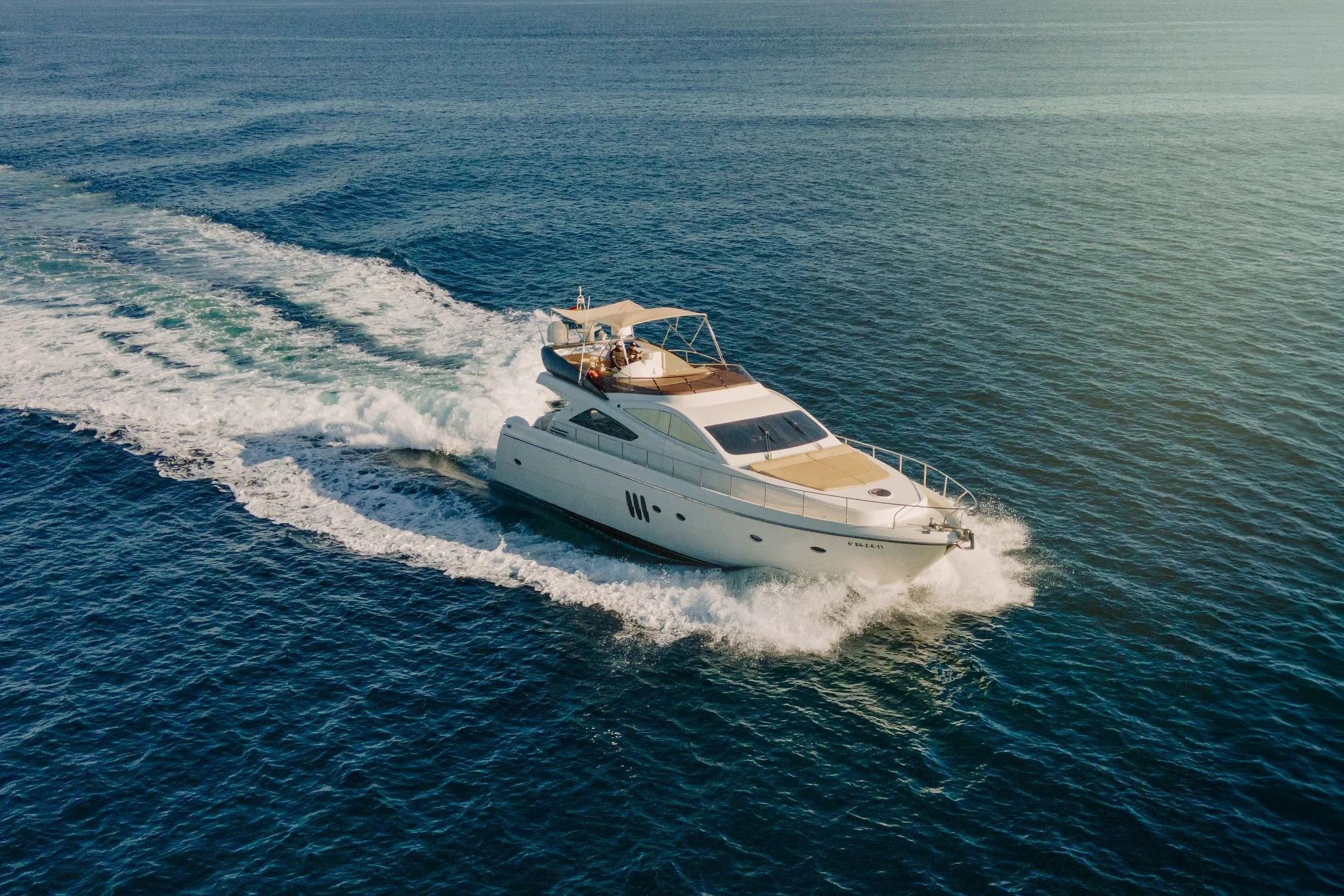 A white yacht cruising through the ocean, creating a wake behind it on a sunny day.