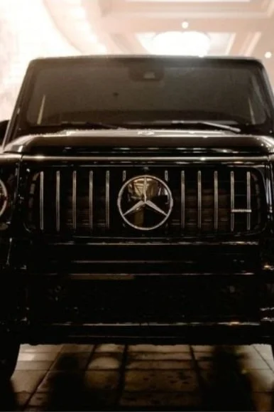 A black vehicle with a clock on its front grille instead of a car emblem, inside a well-lit building.