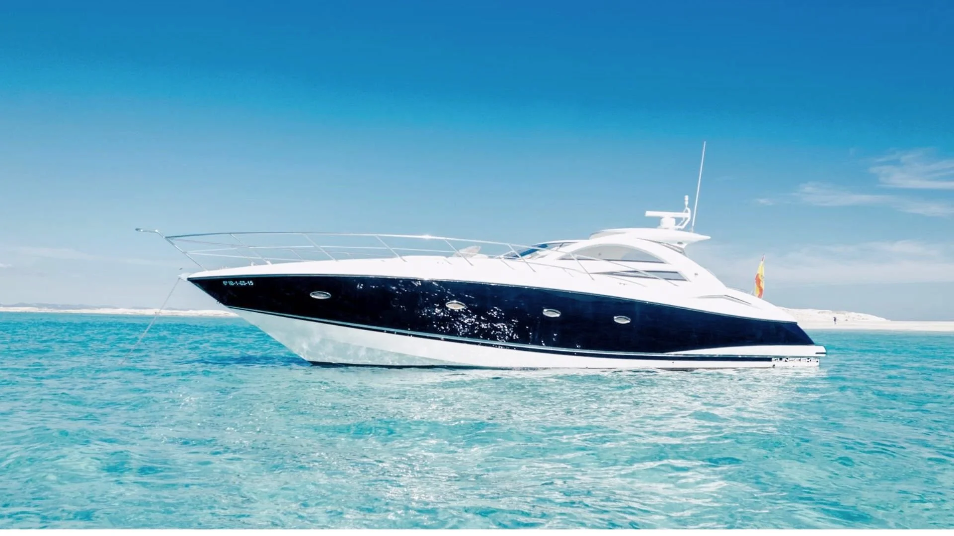 Luxury motor yacht on clear blue water near a sandy shoreline under a bright blue sky.