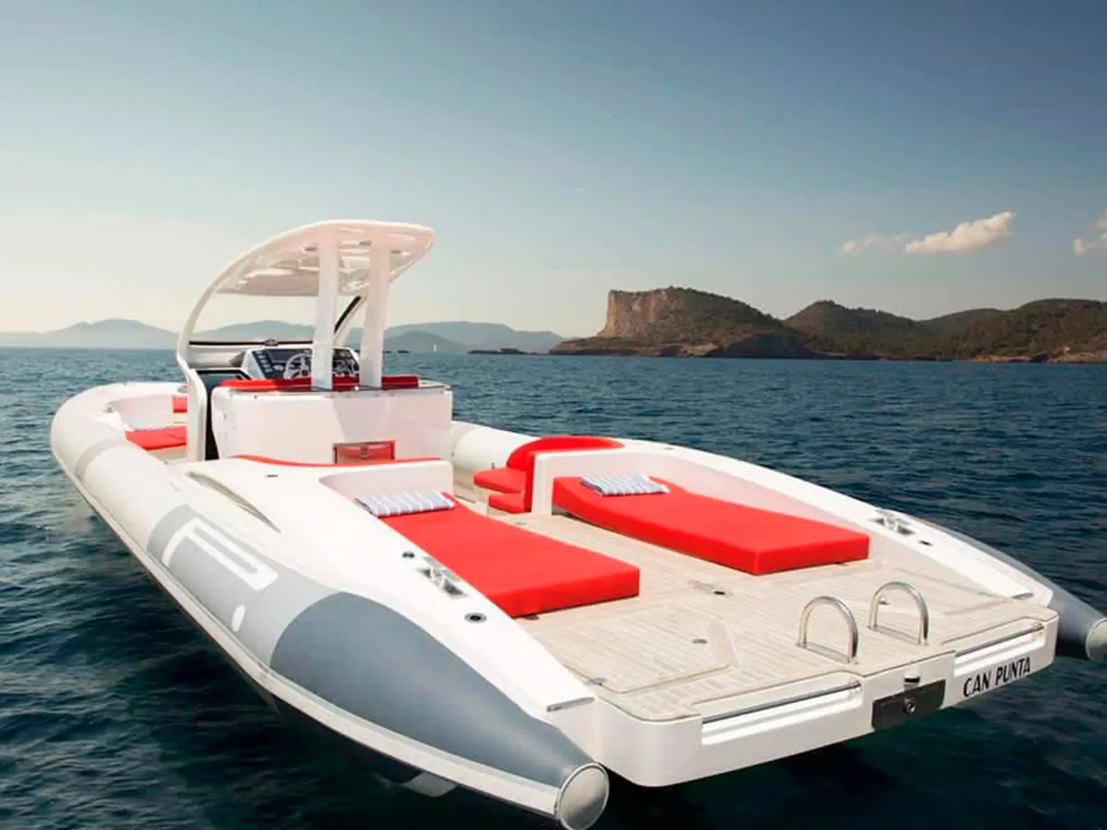Rear view of the Pirelli 1400 showing red sunbeds and open deck layout near the Ibiza coastline