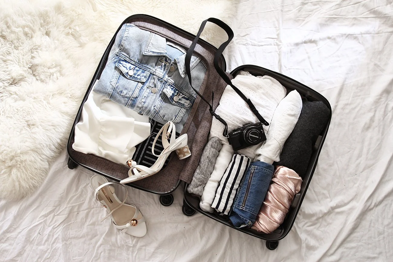 Open suitcase with folded clothes, camera, sandals on bed