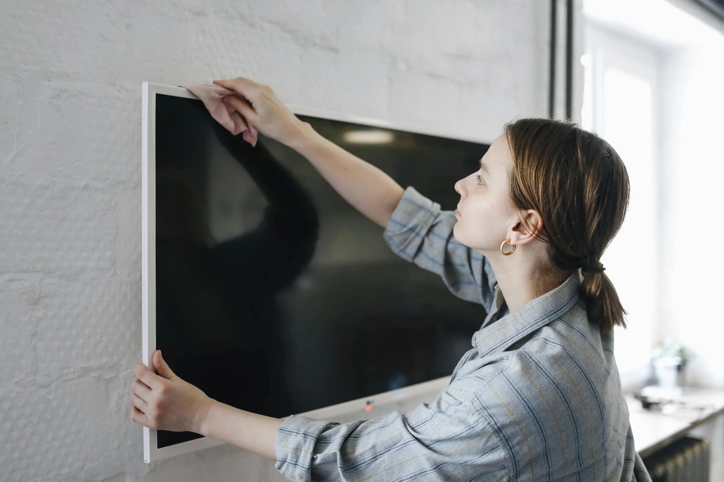 Person cleaning a flat-screen TV mounted on a wall, using a cloth.